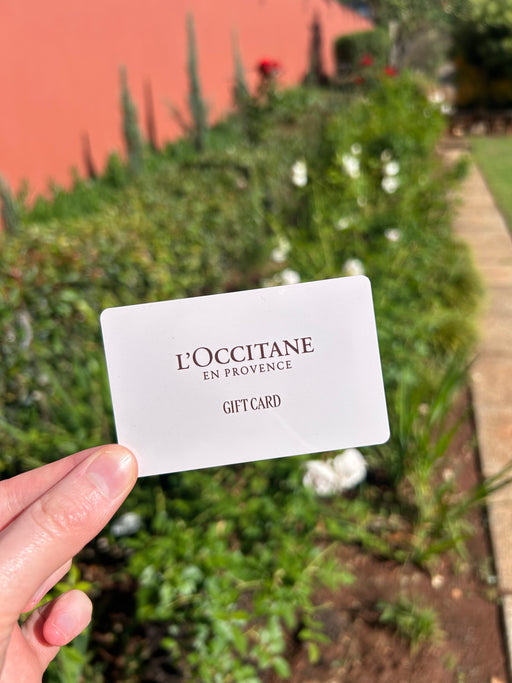 L'Occitane gift card held in front of a garden background